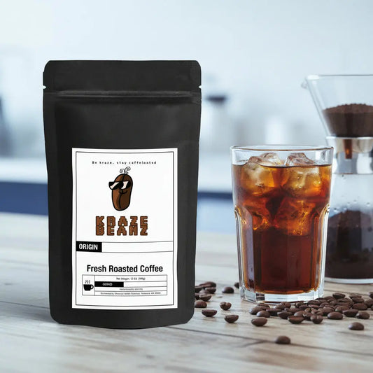 Kraze Beanz Cold Brew Black coffee bag with logon on a label next to a glass of iced coffee on a wooden surface.